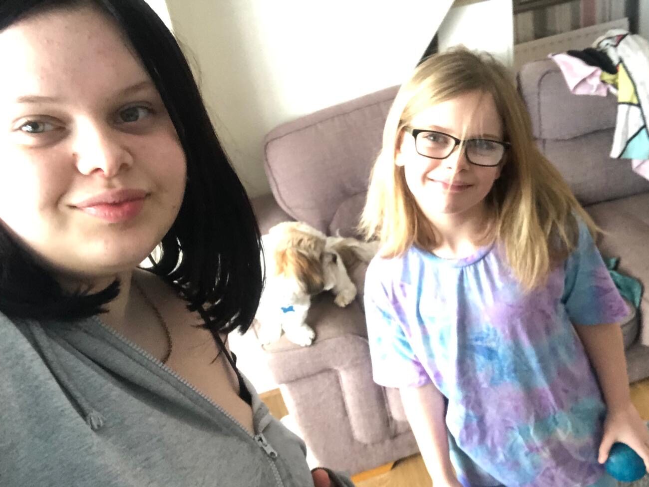 Lucy is holding the camera, looking into the lens and Molly is stood by her side. They are indoors and smiling.