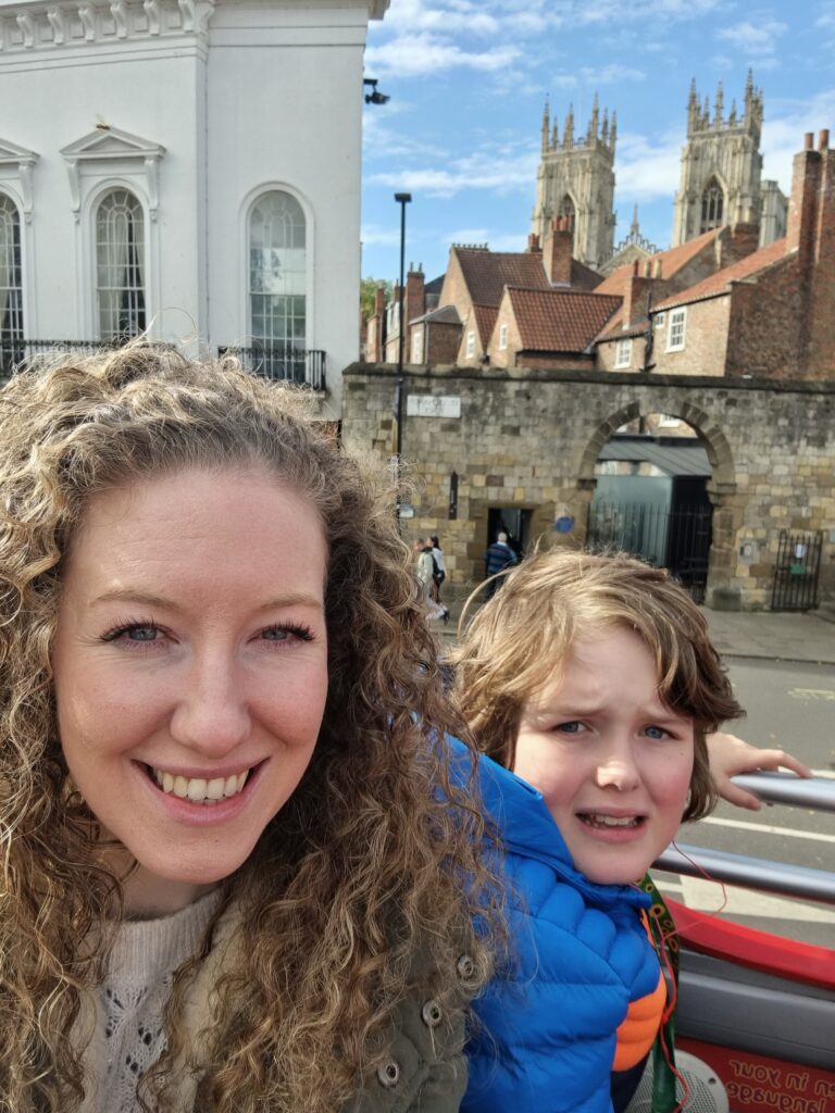 Mum and son take a selfie from the top of an open top bus next to the York city walls.