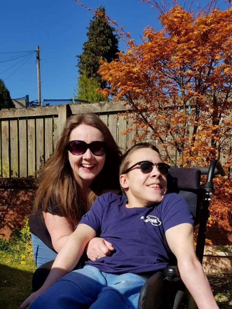 Young man in wheelchair is hugged by his mum in the garden