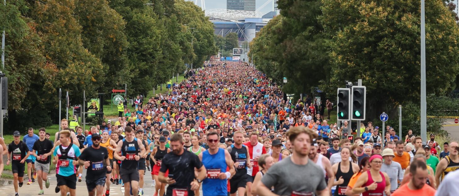 A group of people running down a tree-lined road with a city in the background.