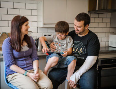 A mother and father with their son in between them, sitting in a kitchen talking