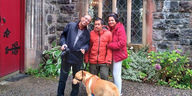 Aaryan, mum, dad and dog stood smiling in front of an old building