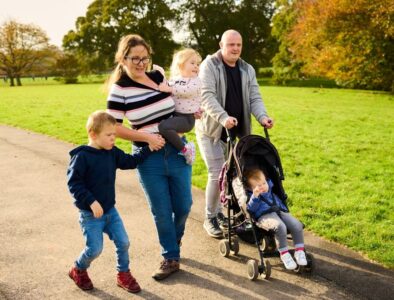A mum and dad walk through a park with their 3 children