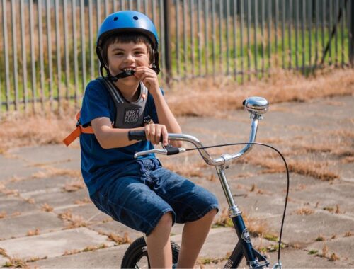 A boy in denim shorts, t-shirt and blue helmet riding a bike