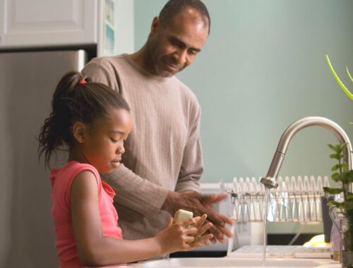 A dad and his daughter washing their hands with a bar of soap at a kitchen sink
