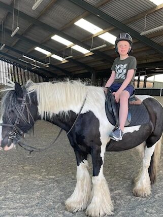 David is sat atop a black and white horse. He is smiling and holding onto the saddle.