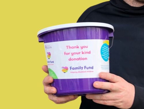 A man in a black hoodie holding a purple Family Fund donation bucket