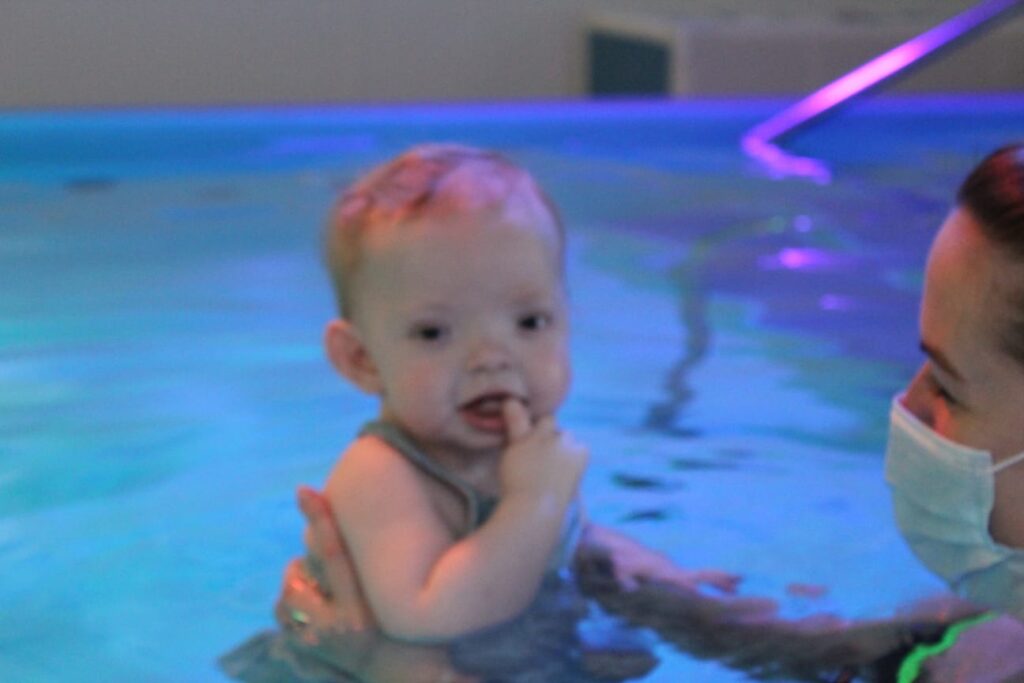 Baby girl is held up in swimming pool