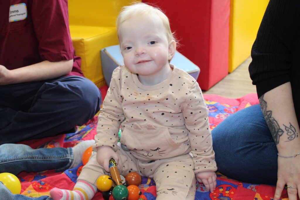 Baby girl holding rattle smiles at the camera