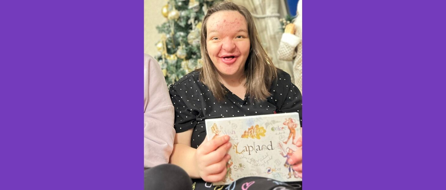 A dark purple background. A photo of a young woman with long dark hair is holding an invitation to Lapland