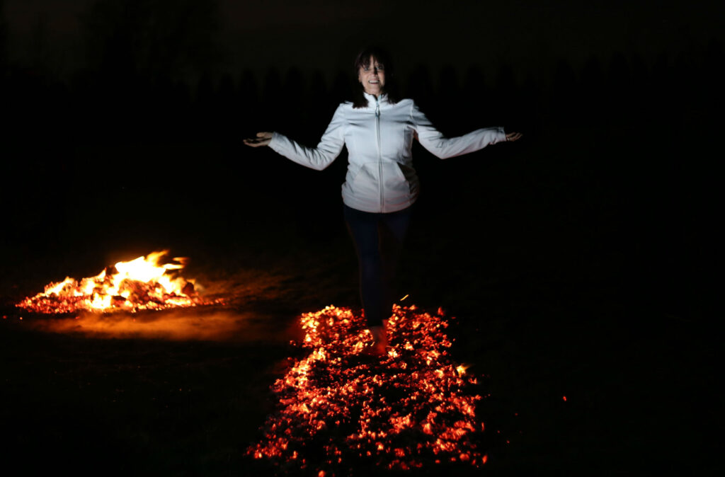 A woman walking across hot coals with her arms out