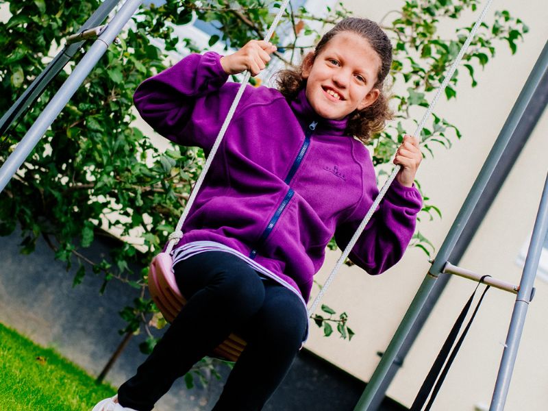 A girl wearing a purple fleece on a garden swing