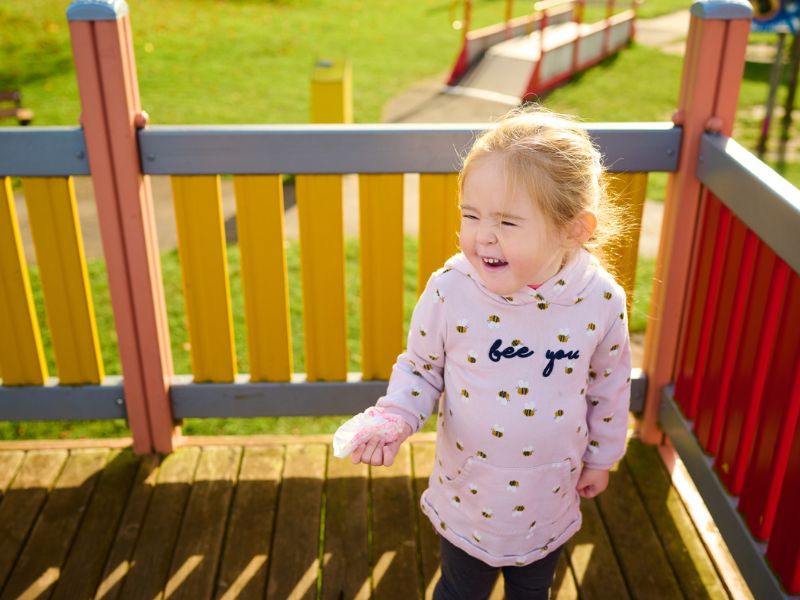 A little girl in a pink hoodie standing on a platform at an adventure park