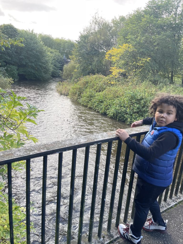 Boy standing on bridge over river looks back at camera