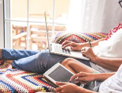 A mum sitting on a sofa with her feet up using a laptop, next to her a boy on a tablet