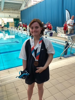 Charlotte stood in front of the swimming pool wearing a medal and smiling.
