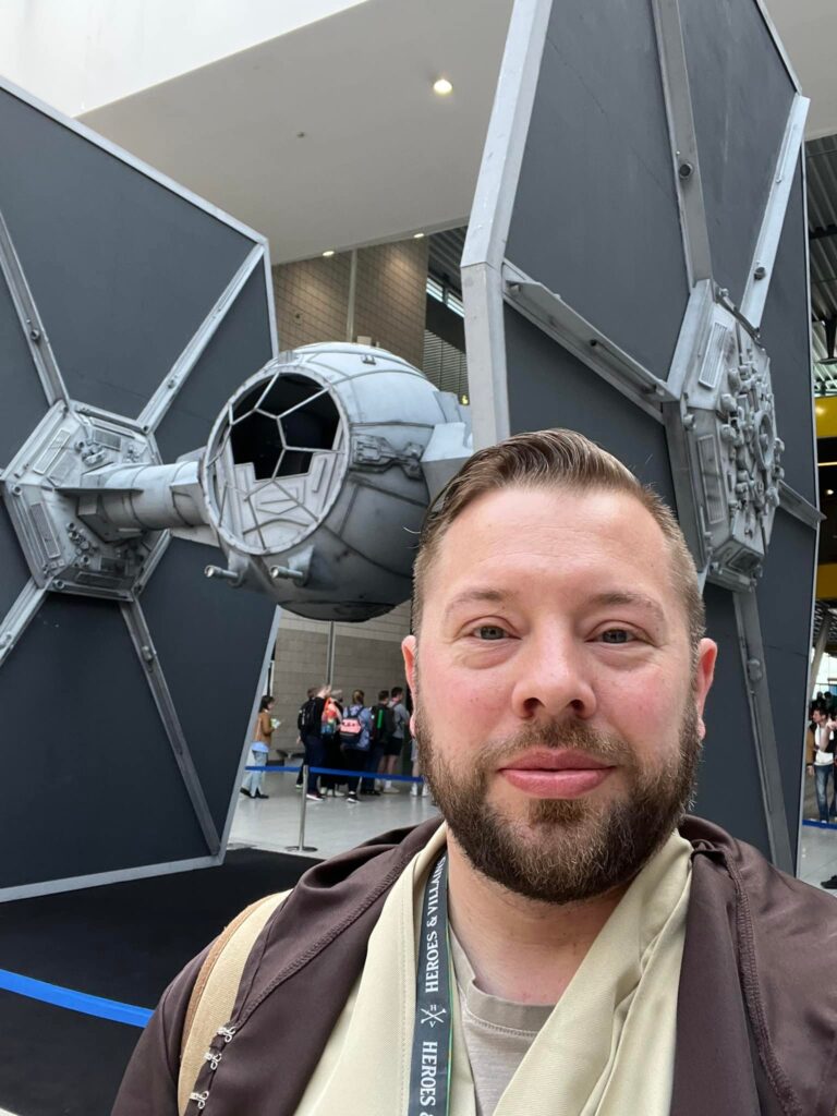 Chris, Family Fund Risk and Compliance Manager, stands in front of a TIE fighter, dressed in Jedi robes.
