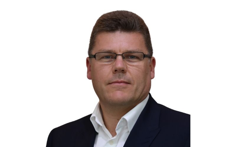 A man with half framed glasses wearing a white shirt and dark blazer