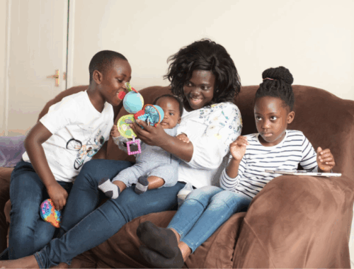 A woman is sat on the sofa holding a little baby. Next to her are sat her son and daughter.