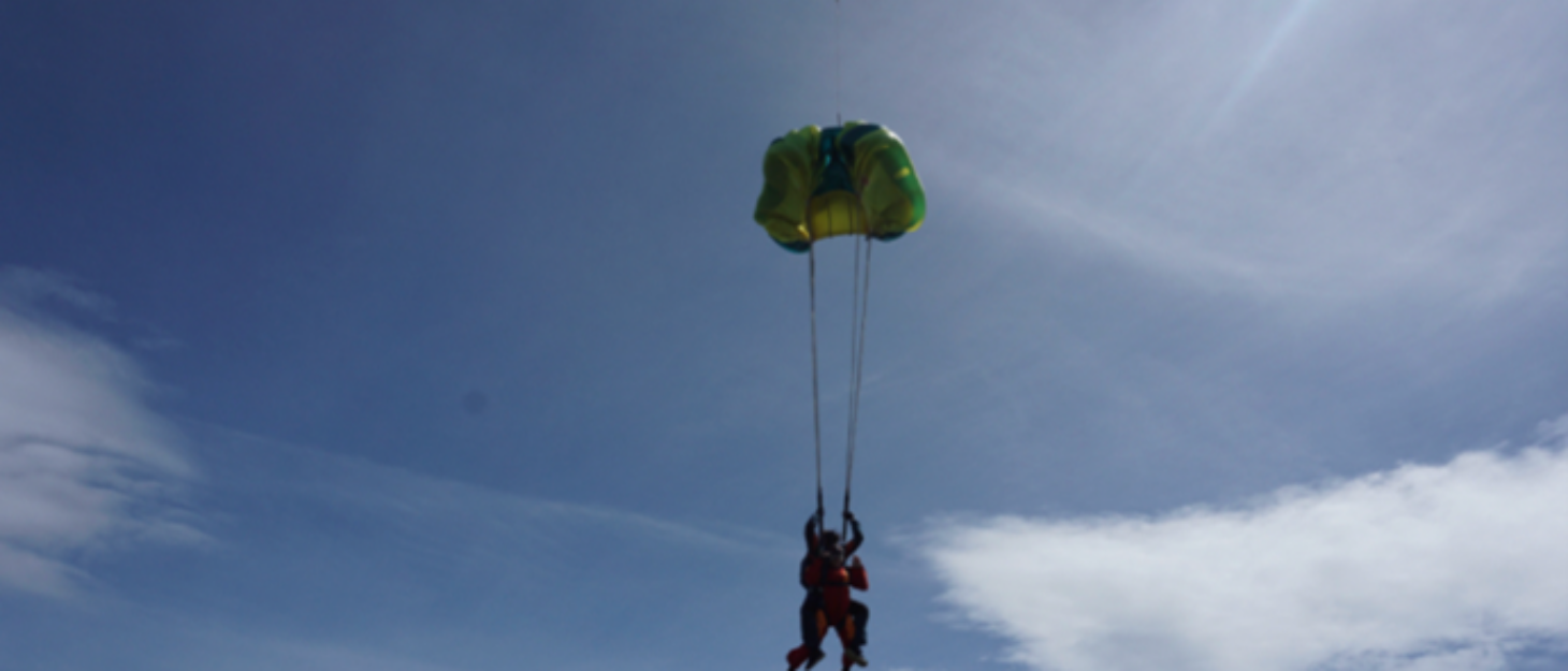 Two people and a parachute opening, silhouetted in the sky