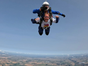 A tandem skydive. The woman is wearing a white Family Fund t-shirt smiling.