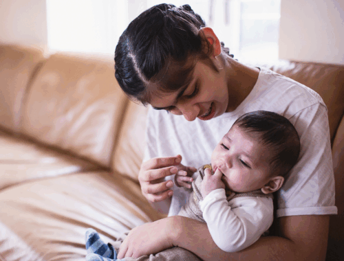 A teenage girl is holding a baby boy in her arms and looking at him.