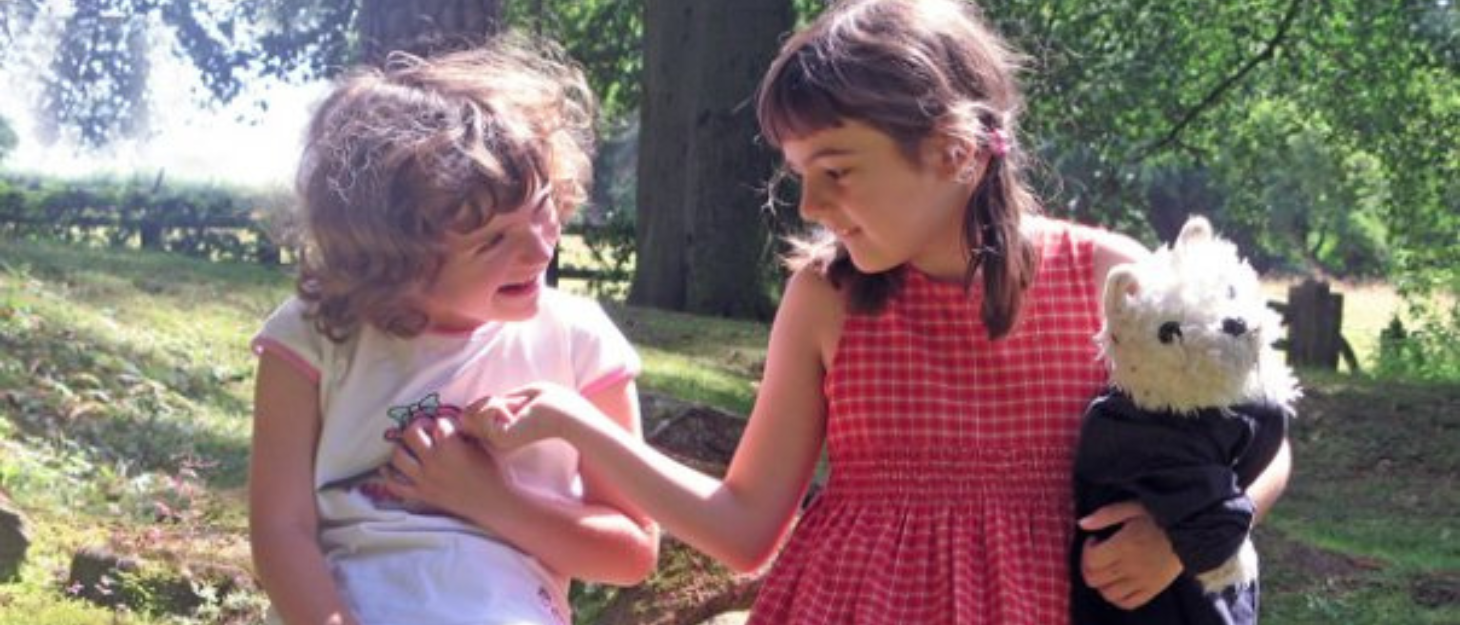 Twin sisters sitting outside playing and tickling each other
