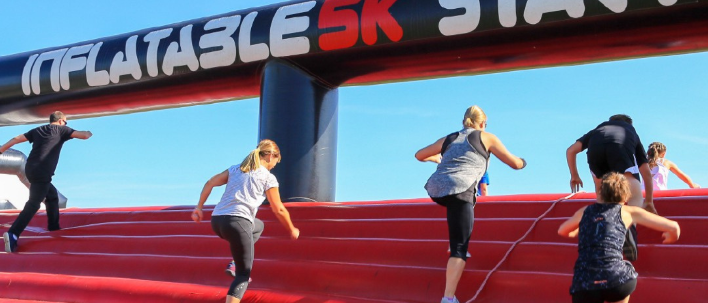 Looking up at a group of people climbing over a large red inflatable on a sunny day