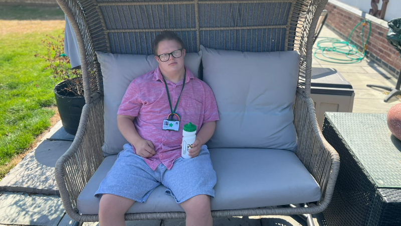 A young adult sits outside on a garden seat