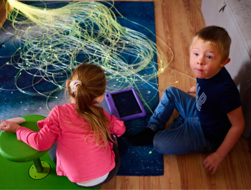 A little girl and her brother sitting on the floor playing with sensory toy string lights