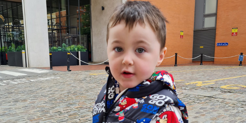 Arthur is wearing a sonic the hedgehog coat and is stood outside. He has short brown hair and he's looking at the camera, with his mouth slightly open.