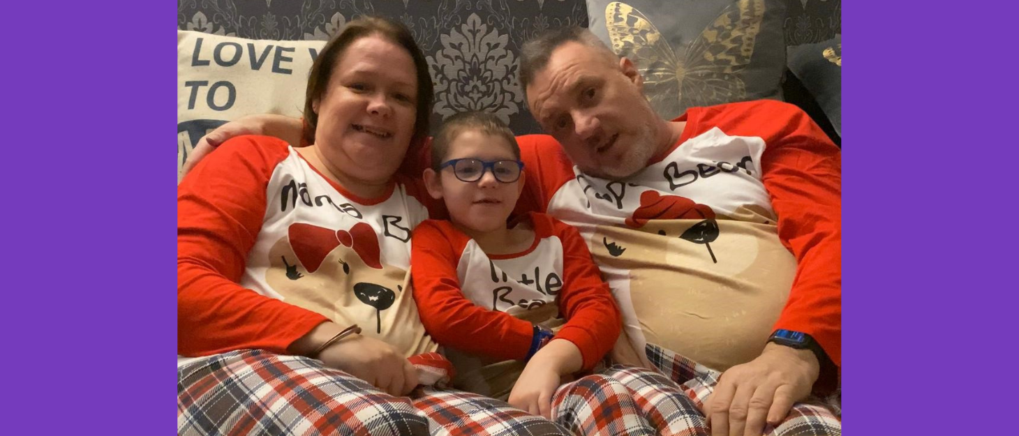 Boy is cuddled by Mum and Dad on the sofa all wearing matching red pyjamas
