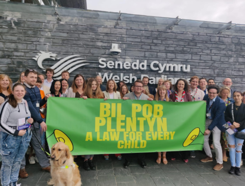 A group of people outside of Welsh Parliament holding a banner saying "Bil Pob Plentyn A law for every child"