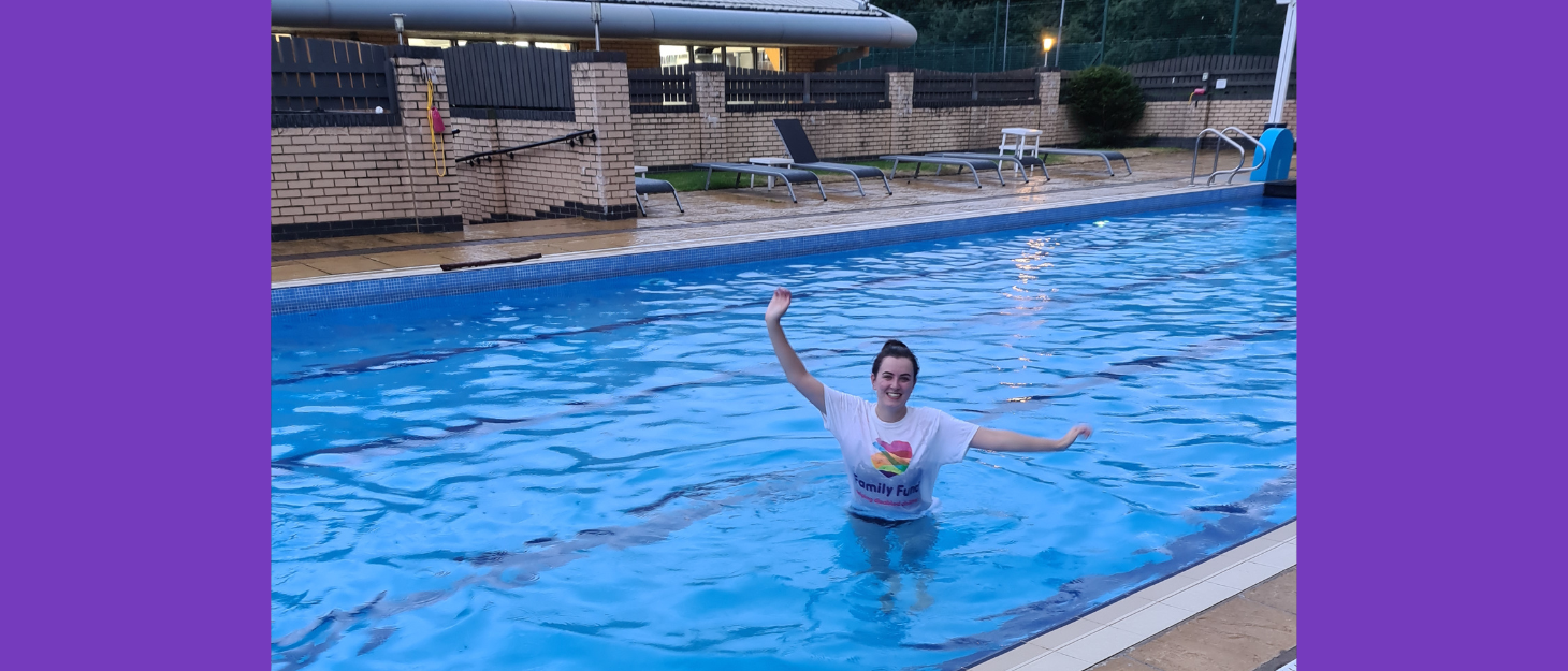 A young woman stands in swimming pool wearing Family Fund t-shirt