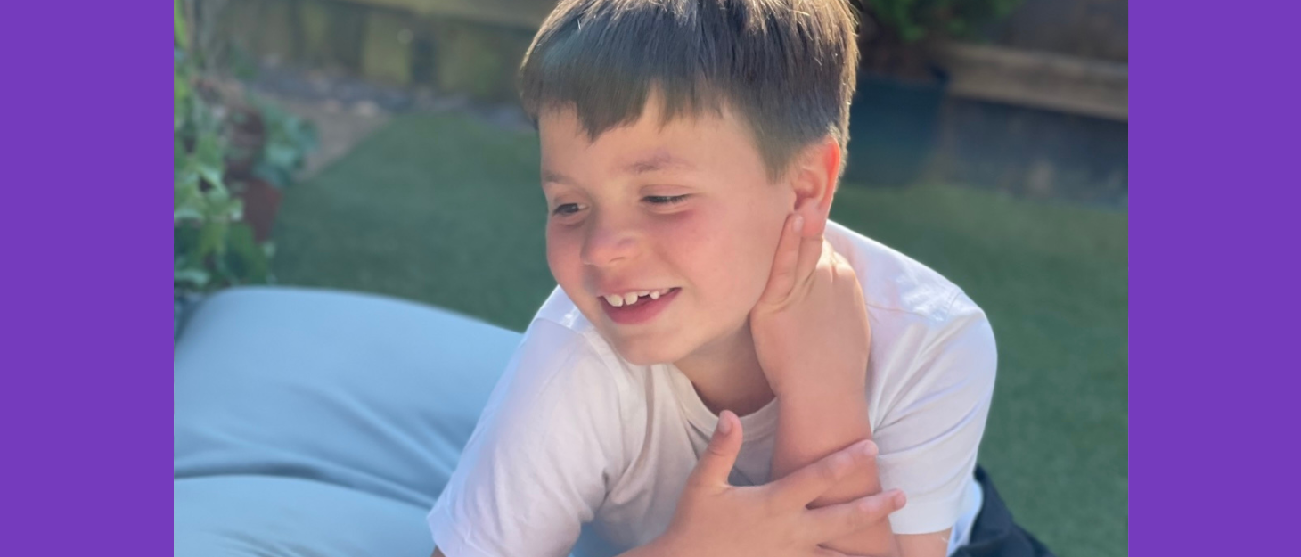 Smiling young boy with brown hair sits on bean bag in garden