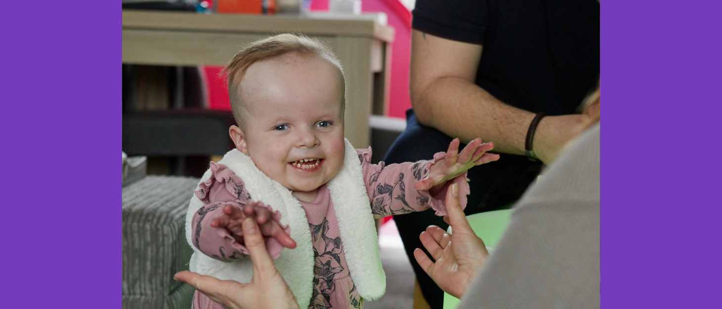 Baby reaches out towards Mum, grinning at camera