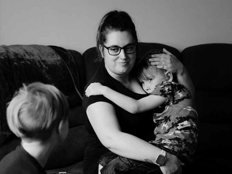 A woman sitting on the sofa with her son on her lap looking toward her other son.