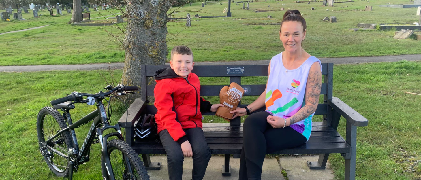Donna and her younger son, Adam, sit together on Ryan's memorial bench. They both hold her golden fundraising glove.