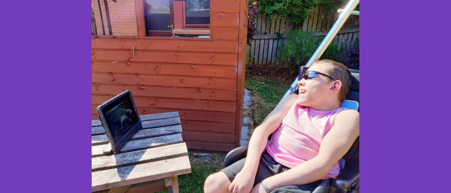 A young man in a wheelchair sat outside watching a video on his tablet