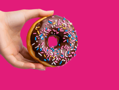 A pink background. On the right, a hand holds a chocolate donut with colourful sprinkles. On the left, white text reads 'WHAT WILL YOU GIVE UP?'