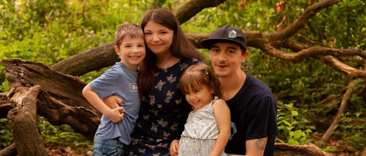 Daniel and Aria are on a family photoshoot with their children Jago and Hazel. They are surrounded by greenery, all close to one another and smiling.