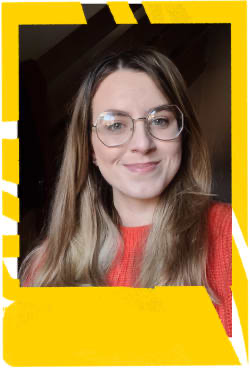 Woman wearing orange jumper and glasses smiles at the camera. 