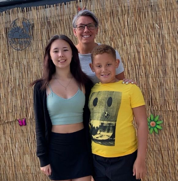 Family photo of mum standing behind her older daughter and younger son, all smiling at the camera