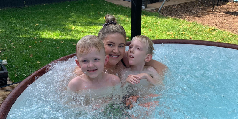 Jess, Mason and Archie are in the hot tub in their garden. Jess is holding both children and they are smiling.