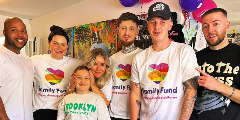 A team of people stand together wearing Family Fund t-shirts. There are balloons and streamers in the background. Everyone is smiling.