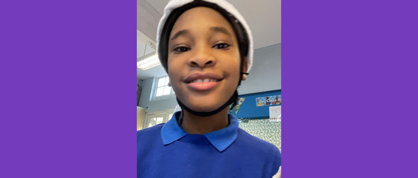 Kalani, a young boy, smiles at the camera. He is at school, wearing a blue uniform.