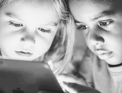 a grayscale image of 2 children looking at an ipad