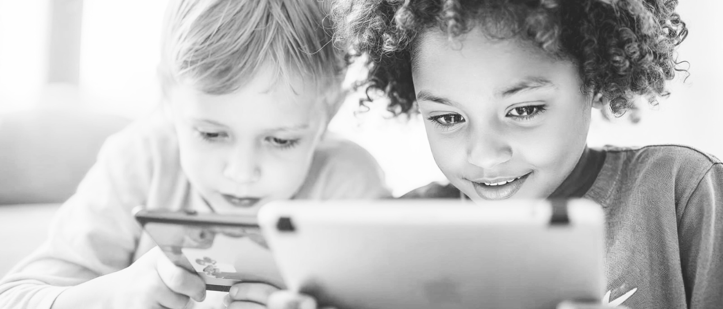 A grayscale image of two children looking at their smart phones