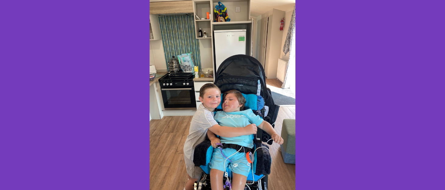 Leo sitting in a pushchair whilst being hugged by a family member.