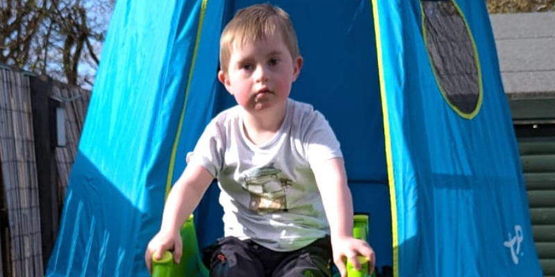 Lewis is at the top of his outdoor play equipment after climbing up the frame, and he's preparing to go down his slide.